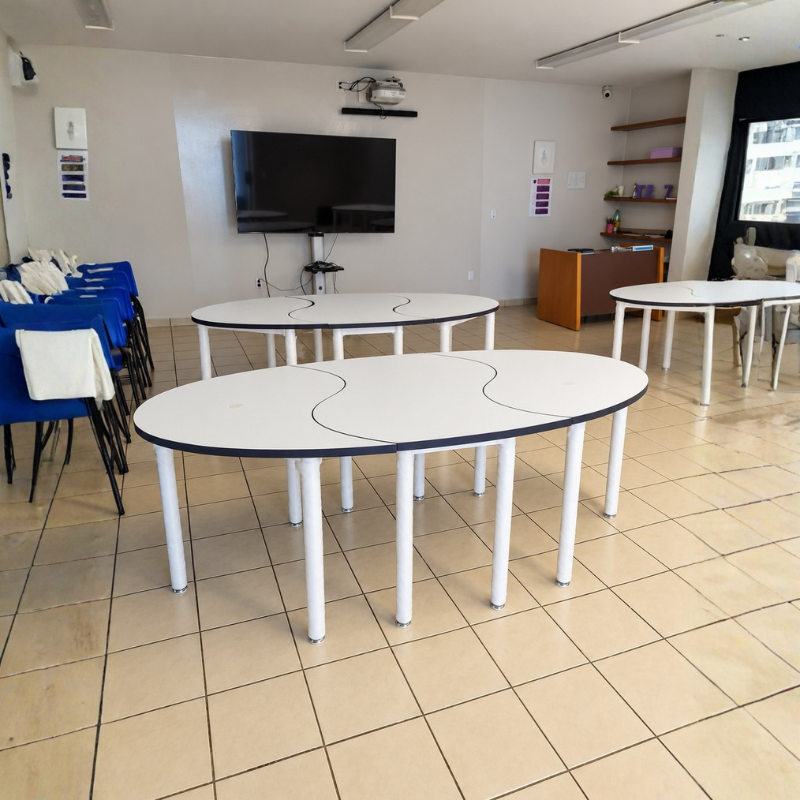 Mesa modular PUZZLE para 6 personas con tres cubiertas curvas ensambladas, estructura tubular blanca y cantos negros, instalada en salón de capacitación.