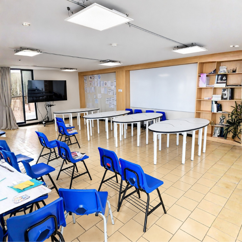 Mesas de trabajo modulares PUZZLE para 6 personas instaladas en aula escolar, con cubiertas blancas, cantos negros y patas tubulares metálicas.